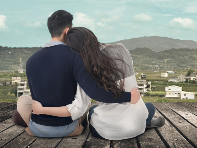 Asian young couple sit and hug together against the sky in outdoor.