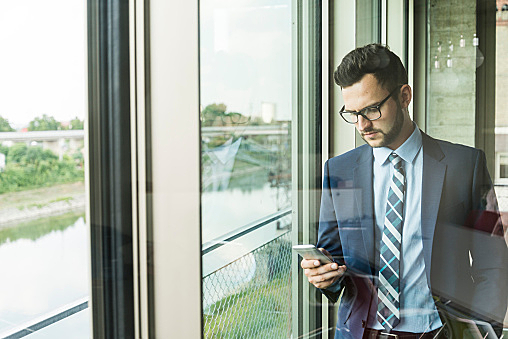 Young businessman at the window looking on cell phone